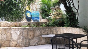 A stone wall with a mural, a small waterfall, and a table with chairs in a garden setting.