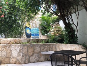 Un muro de piedra con un mural, una pequeña cascada y una mesa con sillas en un jardín.
