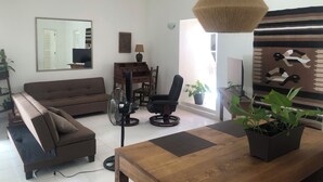 A modern living room with a sofa, a dining table, a fan, and a hanging light fixture.