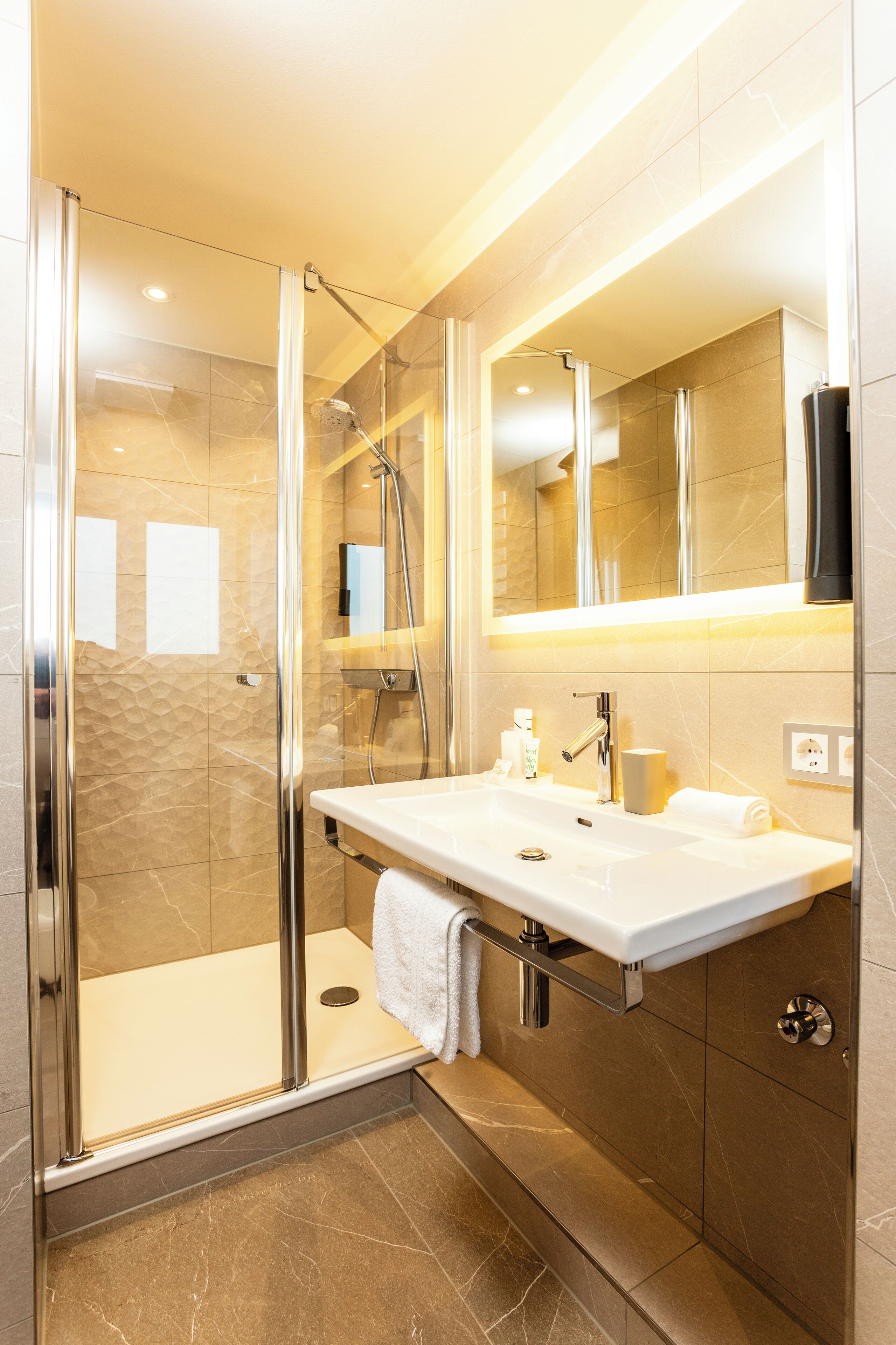 A modern bathroom with a glass-enclosed shower, a white sink with a mirror above it, and a towel hanging on the wall.