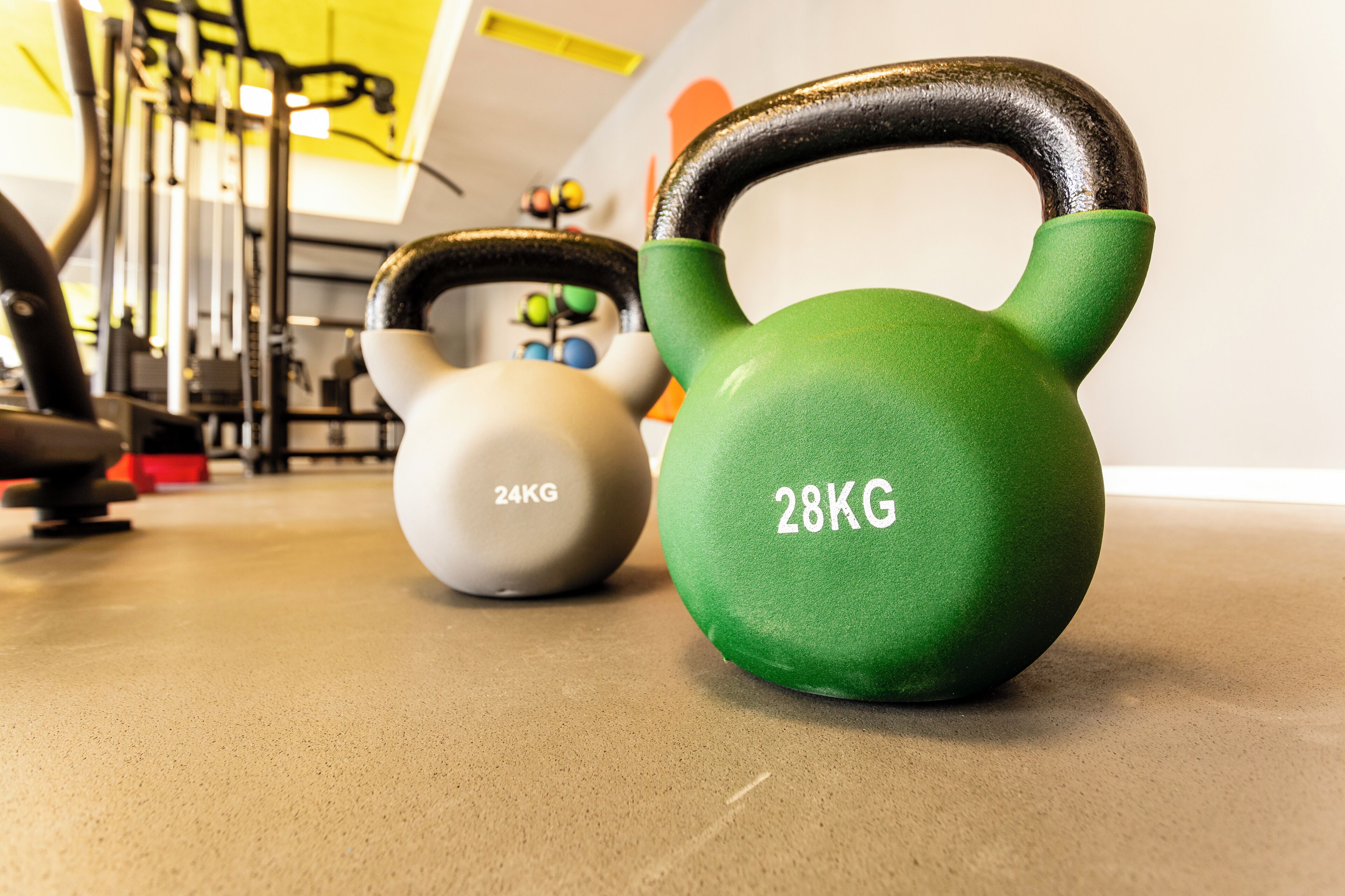 Two kettlebells, one 24kg and one 28kg, on a gym floor with exercise equipment in the background.