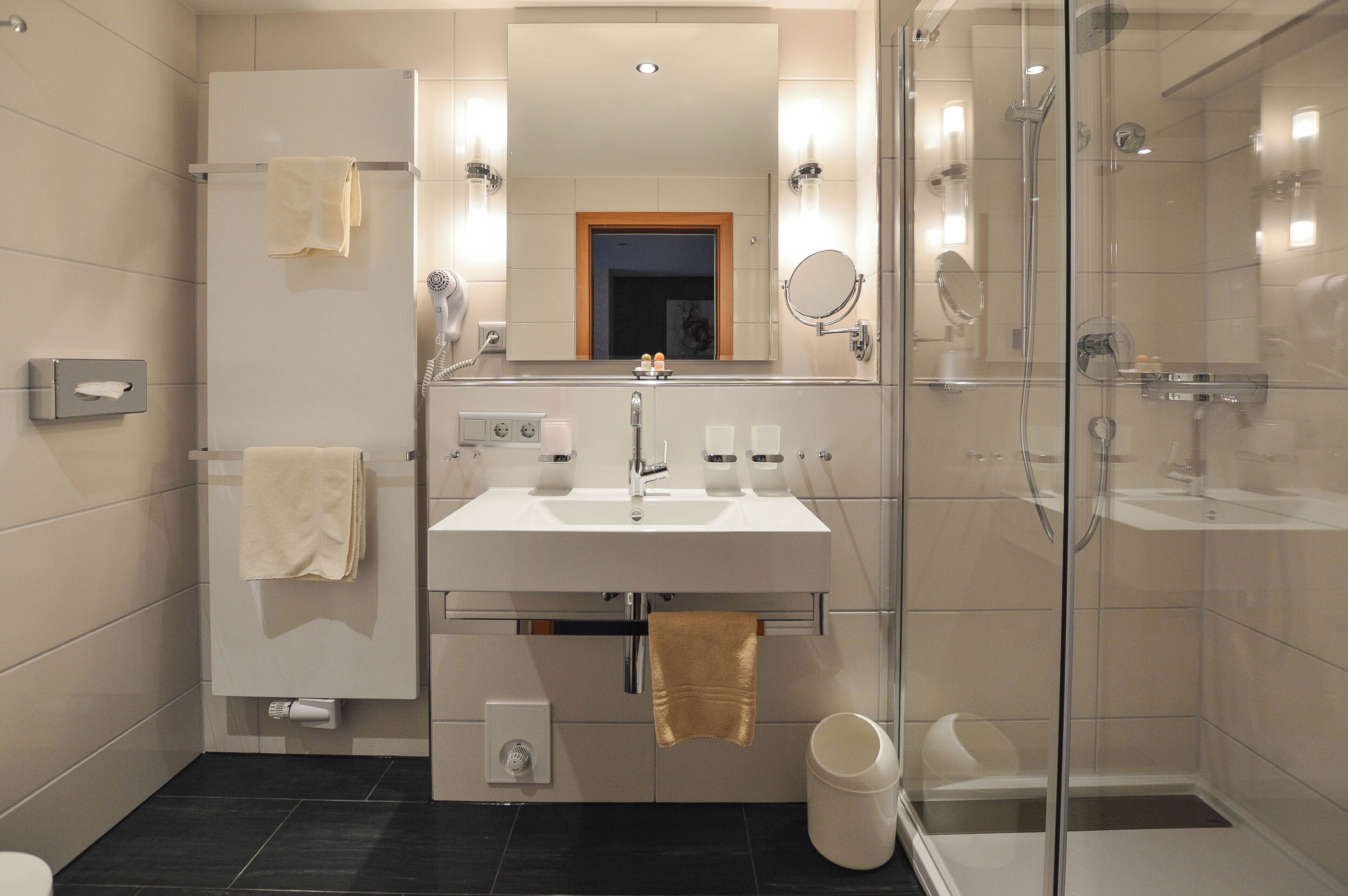 A modern bathroom with a glass-enclosed shower, a vanity with a mirror, and a towel rack.