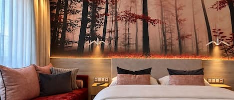 A hotel room with a large bed, a red sofa, and a forest-themed wall mural.