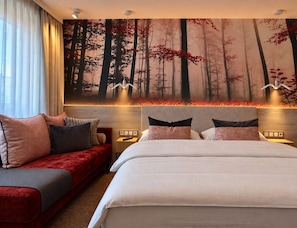Habitación de hotel con una cama grande, un sofá rojo y un mural temático de bosque.