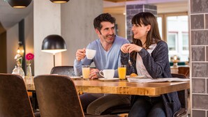 A couple sitting at a wooden table in a cafe with modern pendant lighting and a vase of flowers. - Hotel Böhler (Boeblingen)