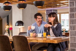 Ein Paar sitzt an einem Holztisch in einem Café, das moderne Pendelleuchten und eine Blumenvase hat.
