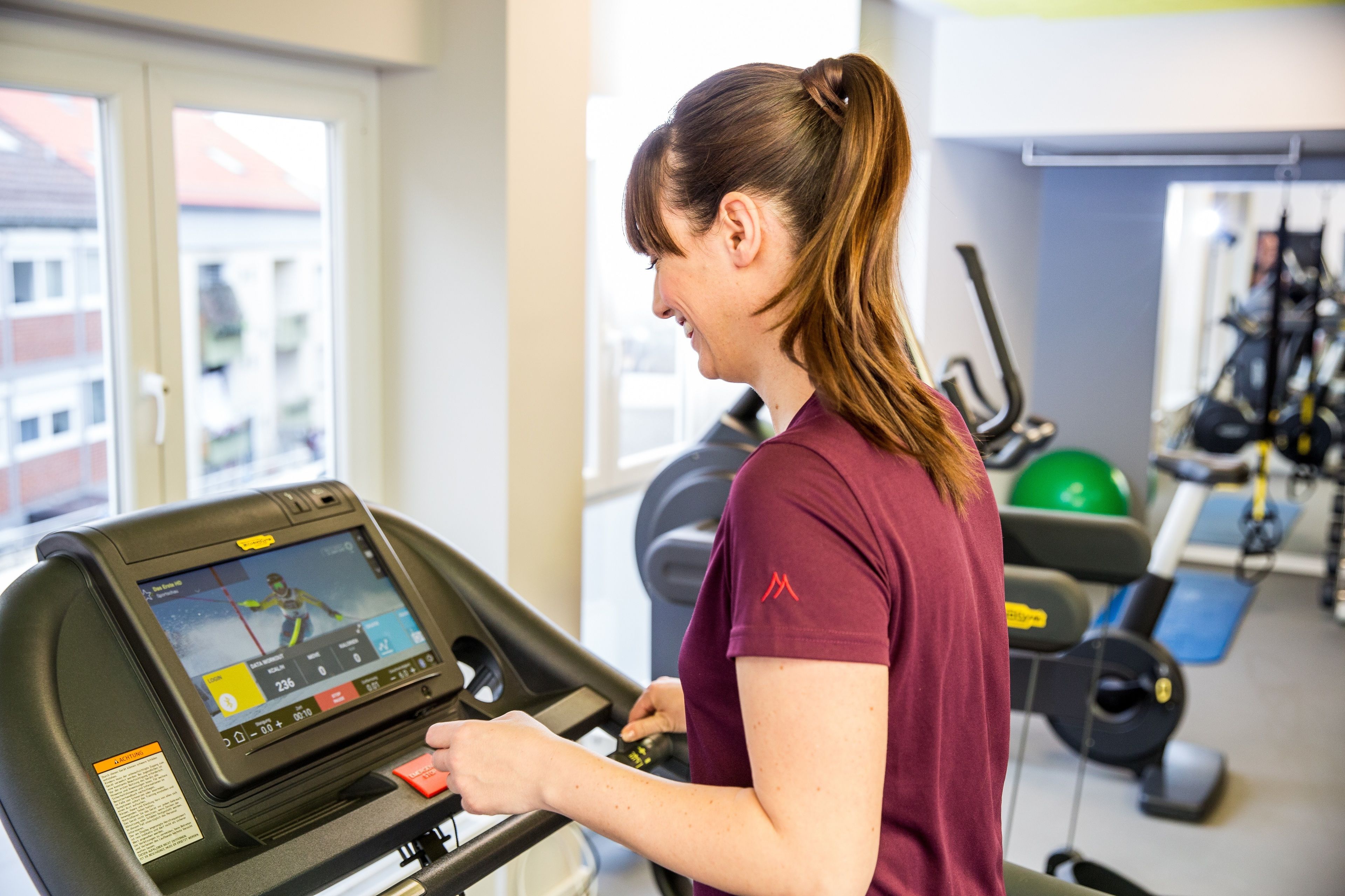 En kvinna som använder ett löpband med en digital display, i ett gym med träningsutrustning i bakgrunden.