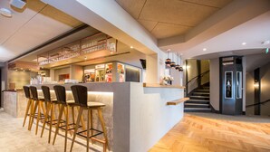 A modern bar area with a counter, stools, and a staircase leading to an upper level. - Hotel Böhler (Boeblingen)
