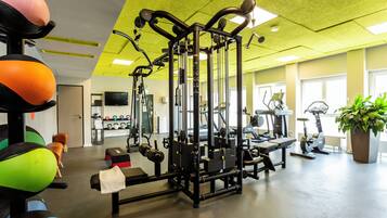 Uma academia com equipamentos de ginástica, televisão e uma grande planta em vaso.