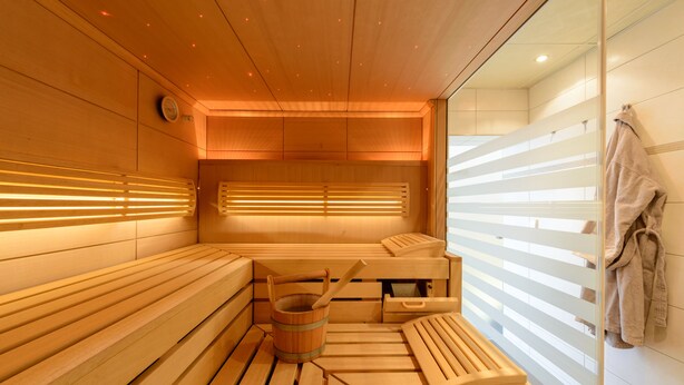 A sauna with wooden benches and benches, a wooden bucket, and a towel rack. - Hotel Böhler (Boeblingen)