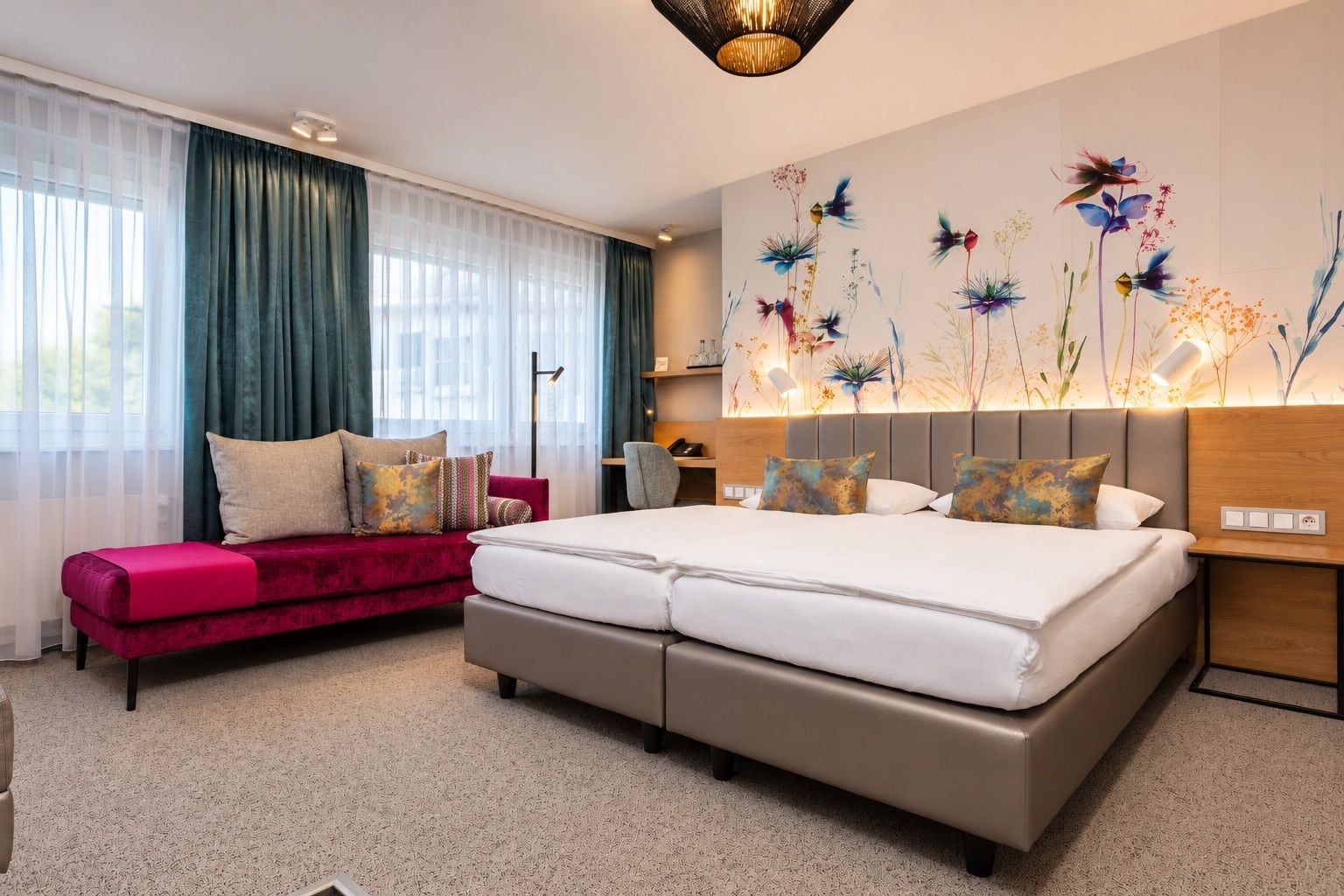 A hotel room with a large bed, a red sofa, a wall-mounted lamp, and a floral artwork.