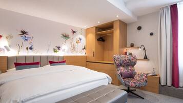 Una habitación de hotel moderna con una cama grande, una zona de estar con un sillón floral, un armario de madera y una pared decorada con motivos florales.