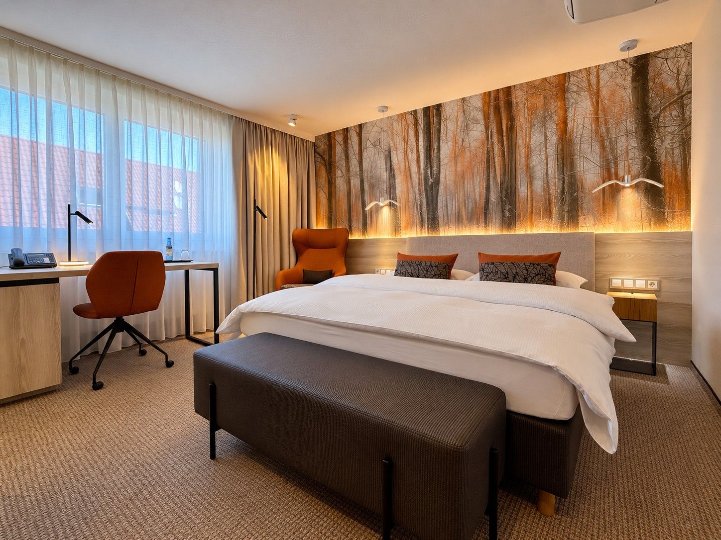 Quarto de hotel com cama grande, escrivaninha, cadeira e parede com mural de floresta.