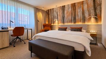 Quarto de hotel com cama grande, escrivaninha, cadeira e parede com mural de floresta.