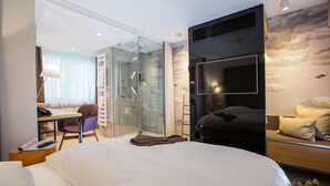 A modern hotel room with a large bed, a desk with a chair, a glass shower enclosure, and a TV mounted on the wall. - Hotel Böhler (Boeblingen)