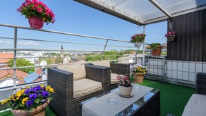 A rooftop terrace with wicker furniture, potted plants, and a clear view of the cityscape. - Hotel Böhler (Boeblingen)