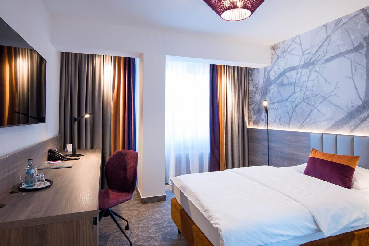 Ein Hotelzimmer mit Bett, Schreibtisch mit Stuhl, Telefon und einer Wasserflasche.
