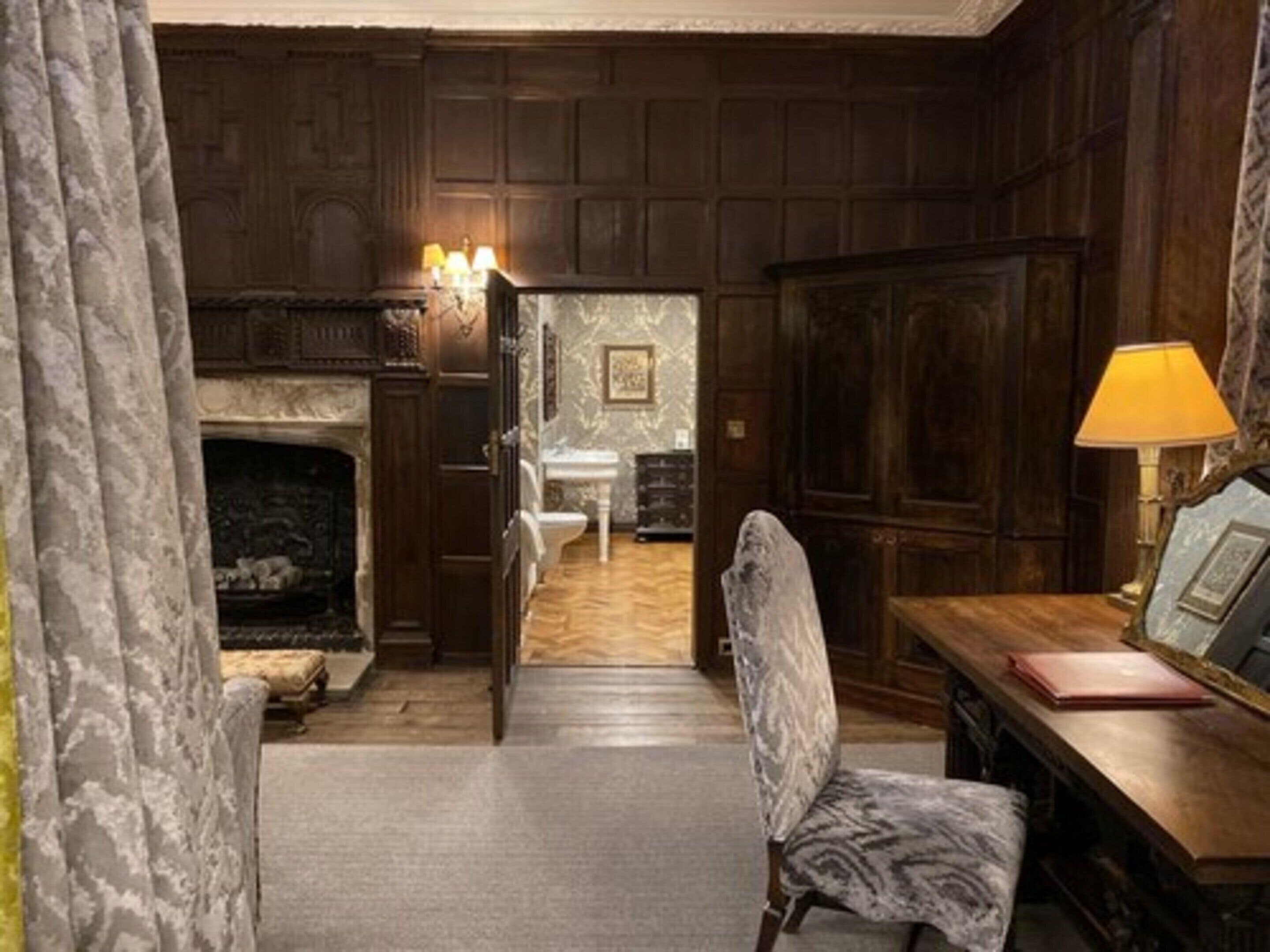 A room with a fireplace, a desk with a lamp, and a chair.
