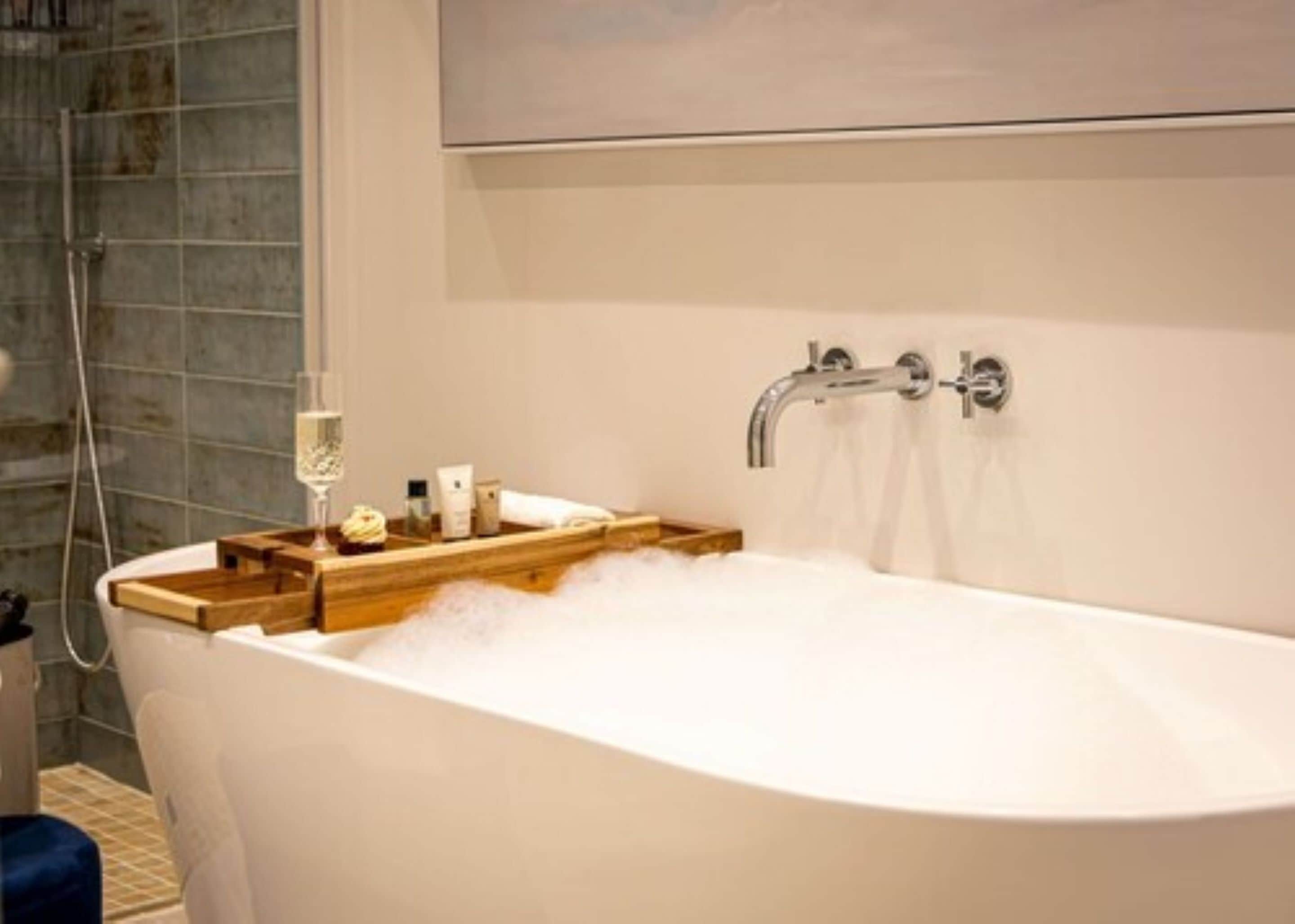 A modern bathroom with a freestanding bathtub, a wooden tray with toiletries, and a shower area with a glass door.