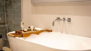A modern bathroom with a freestanding bathtub, a wooden tray with toiletries, and a shower area with a glass door.