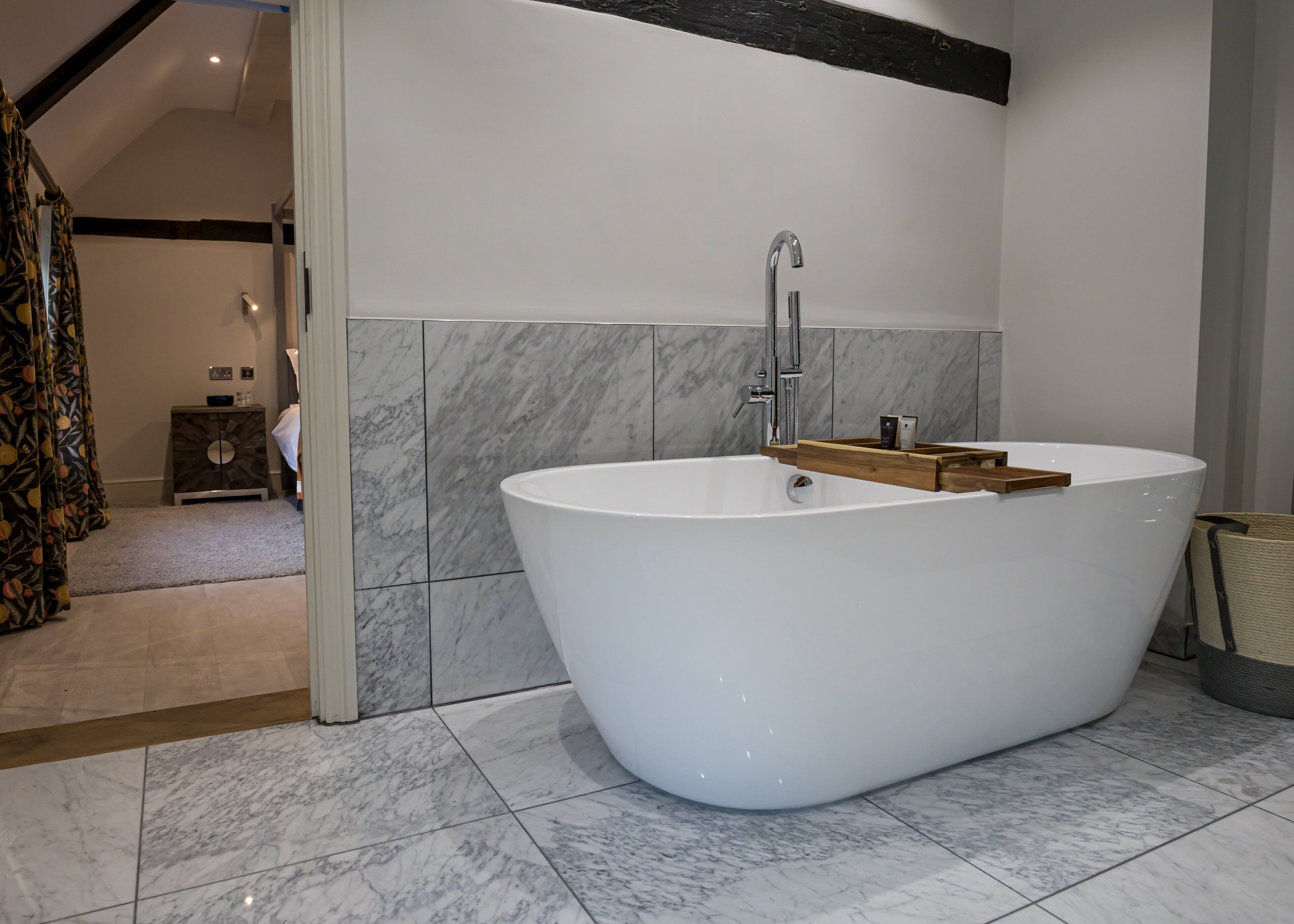 Un baño moderno con una bañera independiente, azulejos de mármol y un aparador de madera.