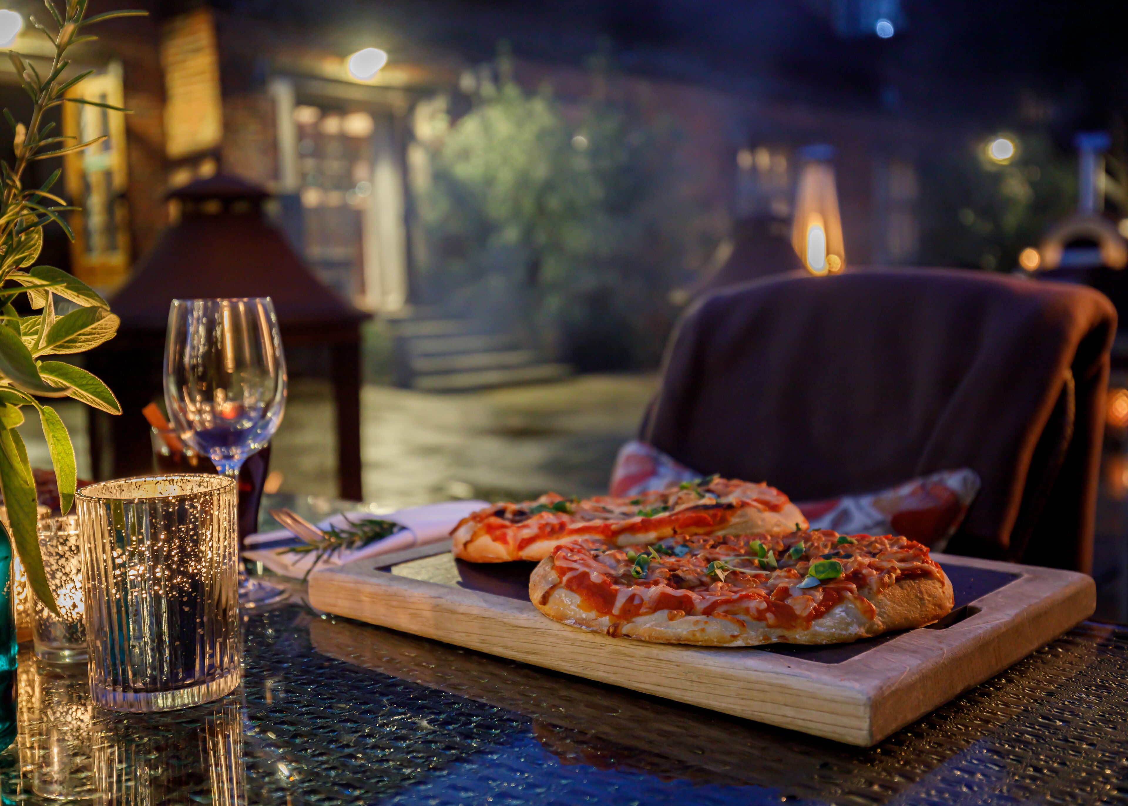 A dining table with two pizzas, a glass of red wine, and a candle.