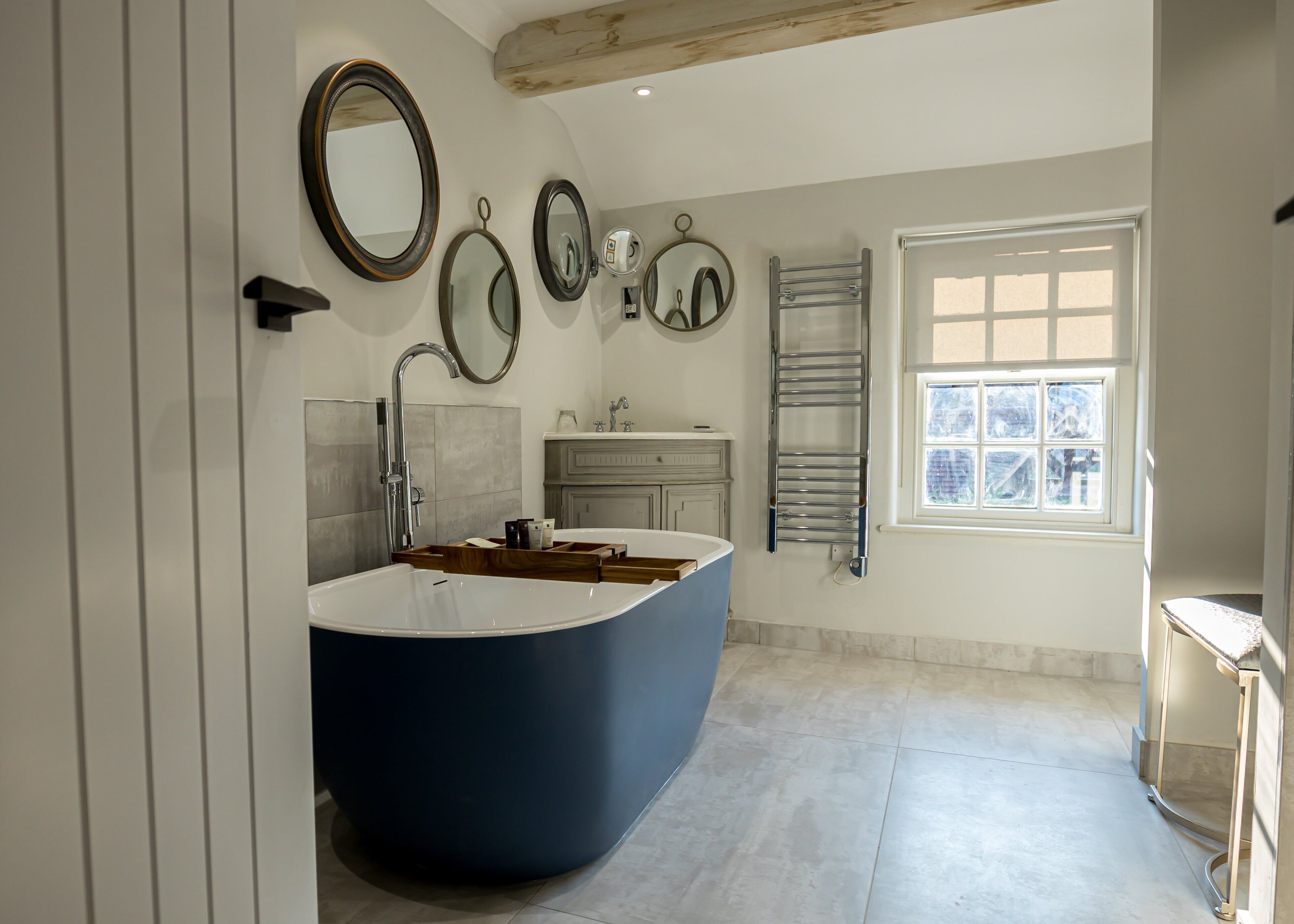 Een moderne badkamer met een groot bad, meerdere spiegels, een handdoekhouder en een raam dat voor natuurlijk licht zorgt.