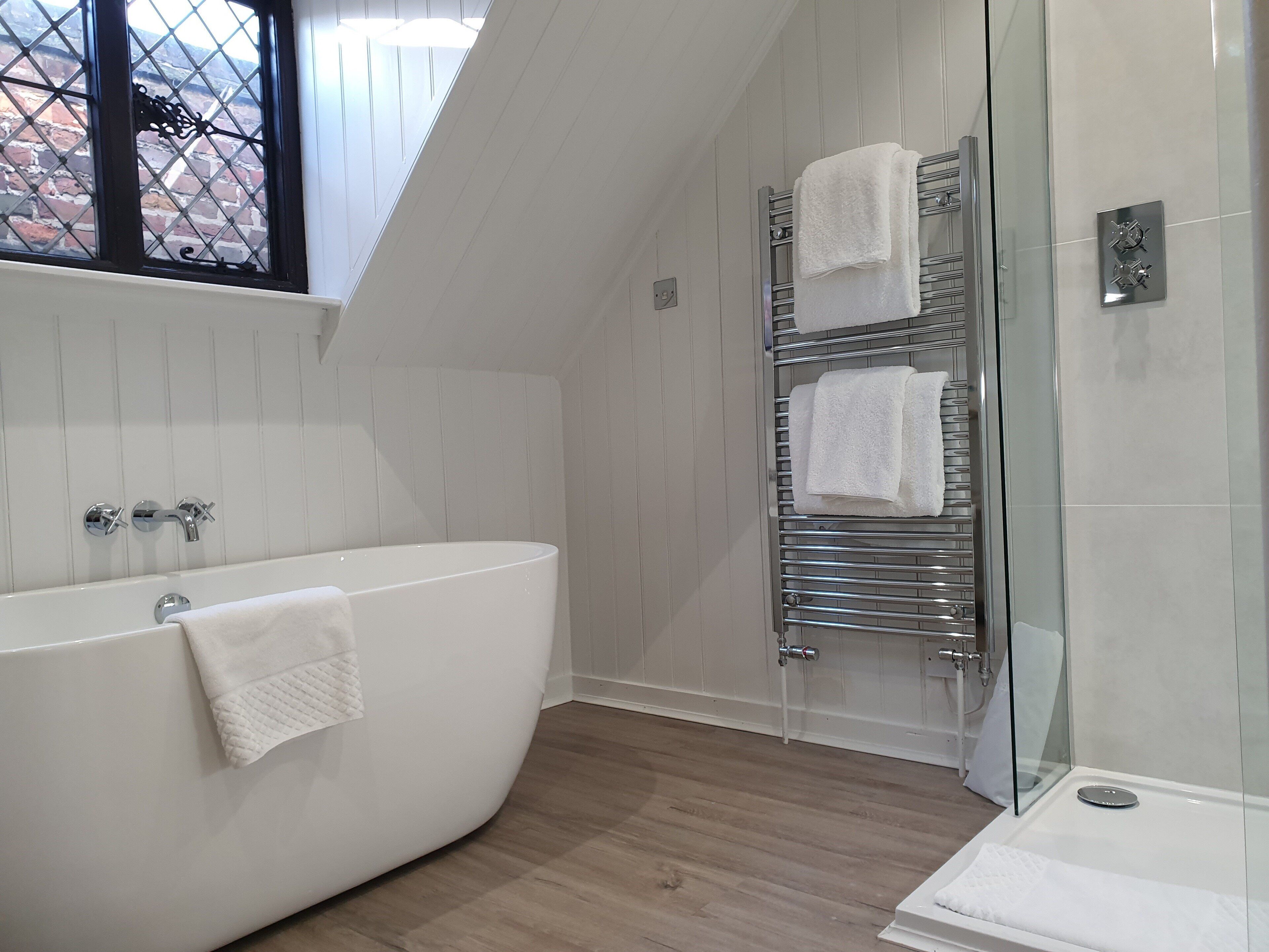 A modern bathroom with a freestanding bathtub, a glass shower enclosure, and a towel rack with multiple towels.