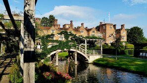 Un edificio histórico con un puente sobre un canal, rodeado de jardines y árboles bien cuidados.