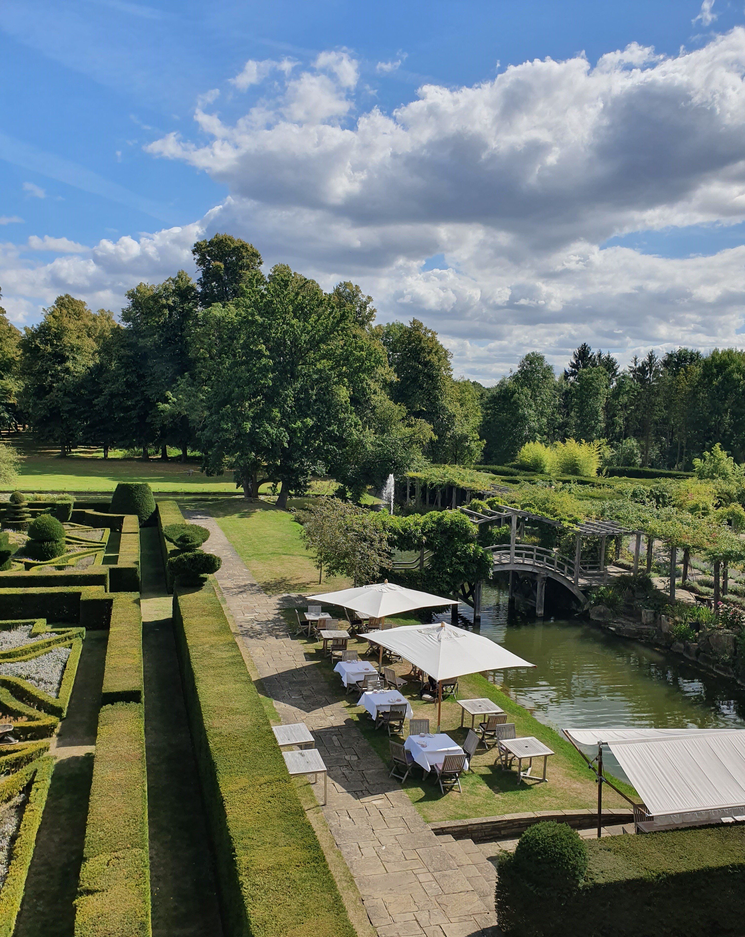 A landscaped garden with a pond, a bridge, and outdoor seating with umbrellas.