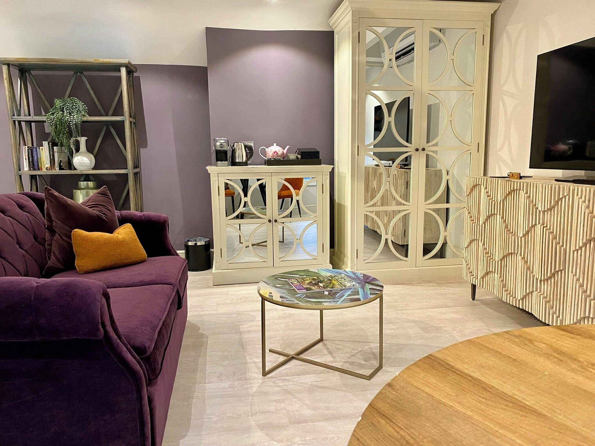 A living room with a purple sofa, a coffee table, a cabinet with glass doors, and a television on a stand.