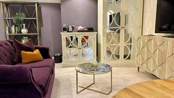 A living room with a purple sofa, a coffee table, a cabinet with glass doors, and a television on a stand.
