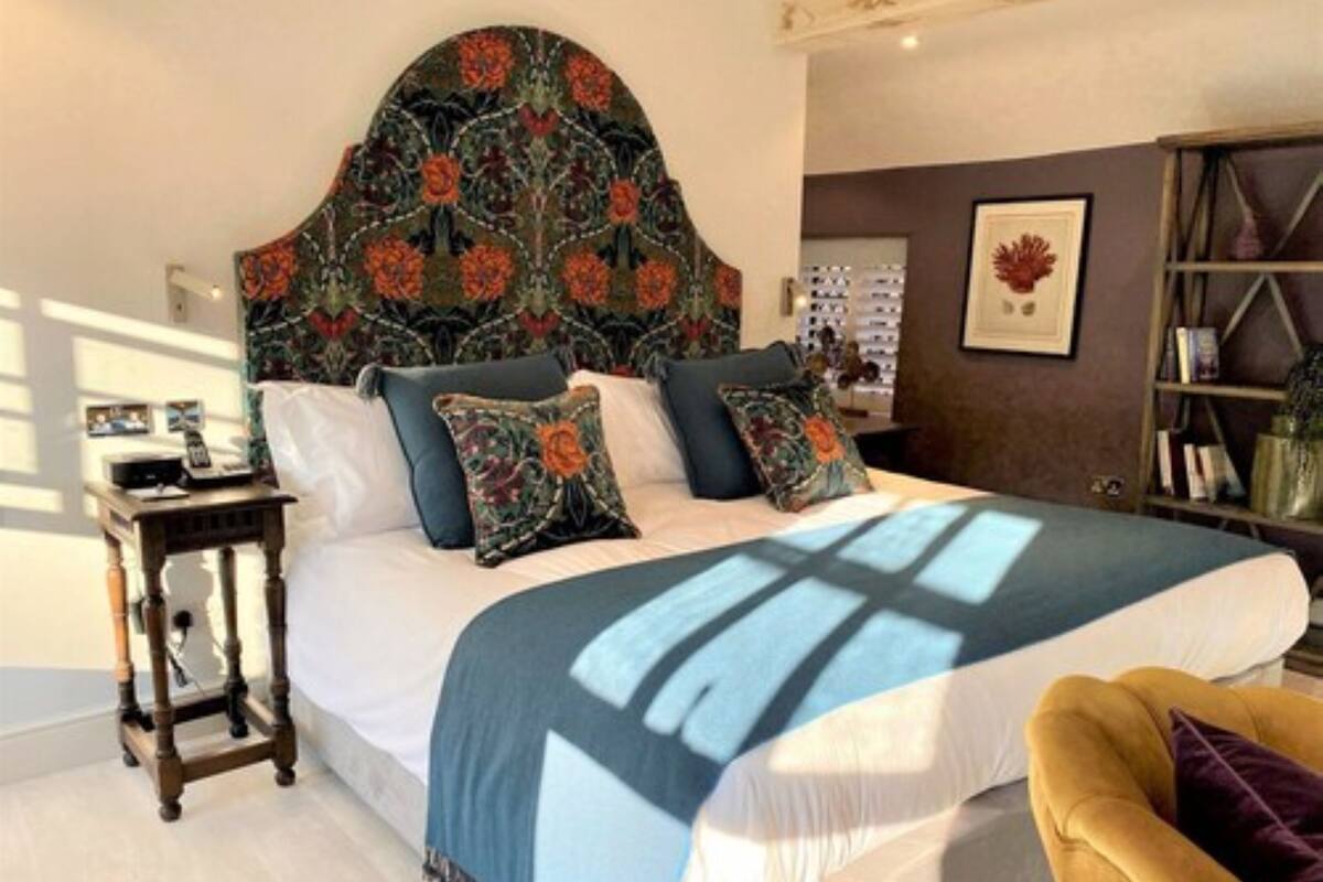 Un dormitorio con una cama grande, una mesita de noche de madera, un sillón amarillo y una estantería.