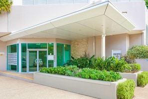 A modern building entrance with a covered waiting area, a glass door entrance, and a fire control sign. - Beachlife Holiday Apartments (Darwin)