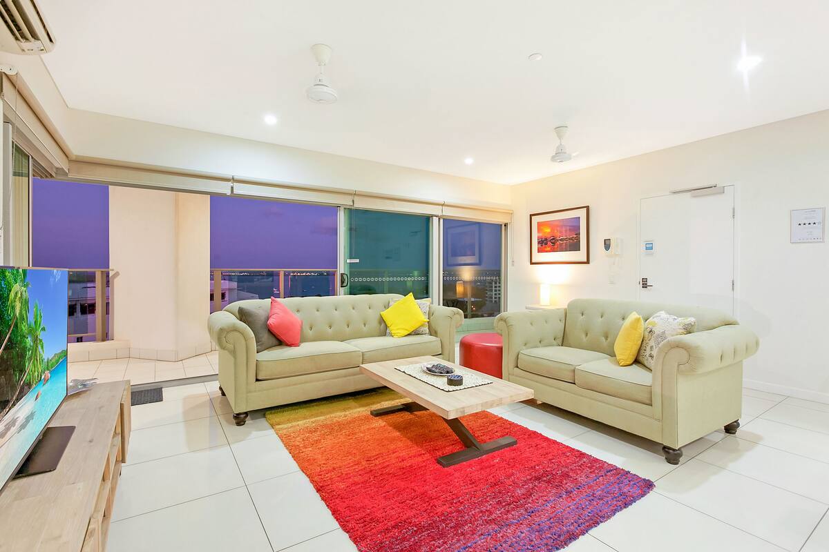 Una sala de estar moderna con un sofá seccional color beige, una mesa de centro de madera y una alfombra colorida.