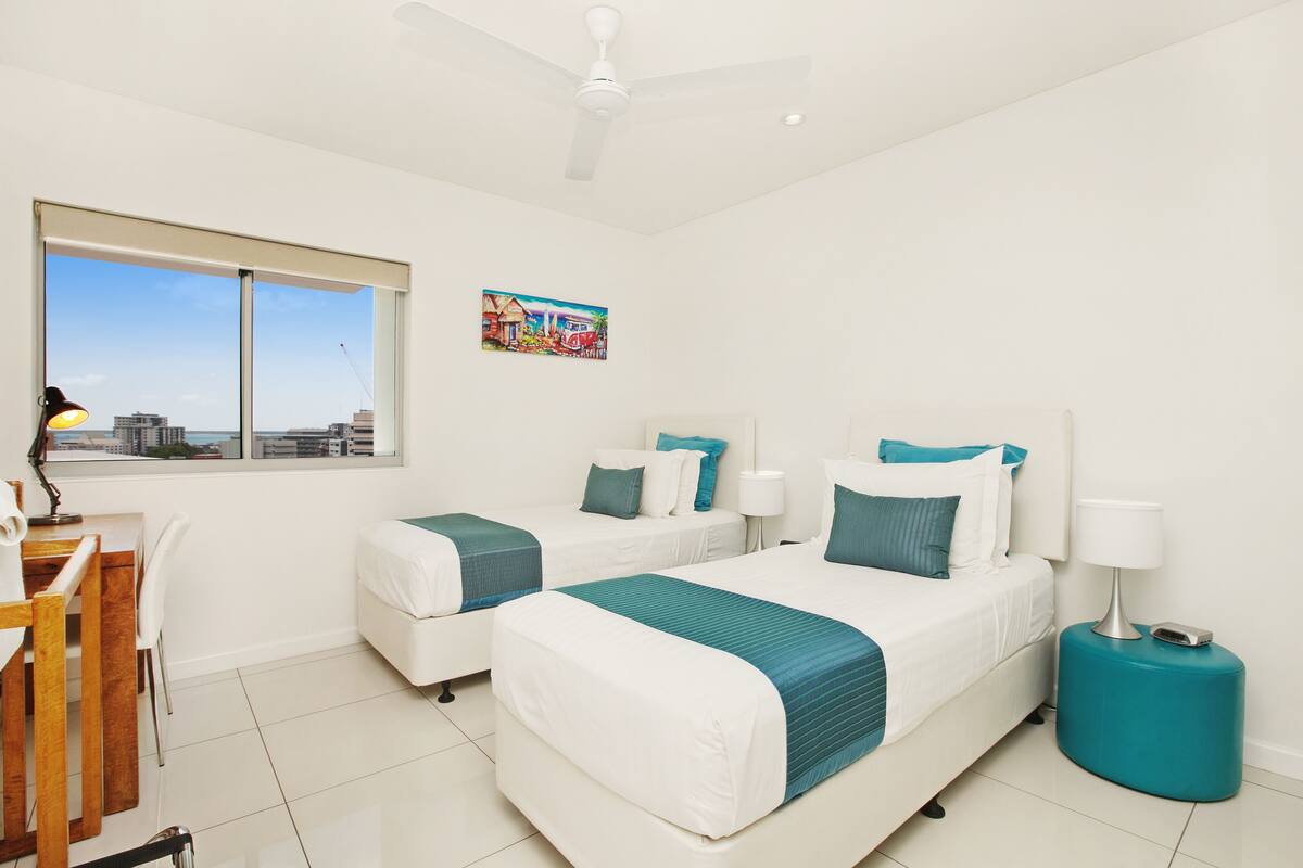 Habitación de hotel con dos camas, un escritorio y una ventana con vistas a la ciudad.