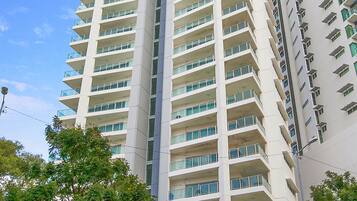 A high-rise hotel with multiple balconies, a gated entrance, and surrounding greenery.