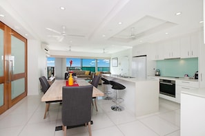 Une cuisine moderne avec des meubles blancs, un îlot central et un coin repas comprenant une table et des chaises en bois.