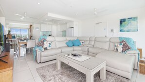A modern living room with a sectional sofa, a coffee table, and a dining area with a table and chairs. - Beachlife Holiday Apartments (Darwin)