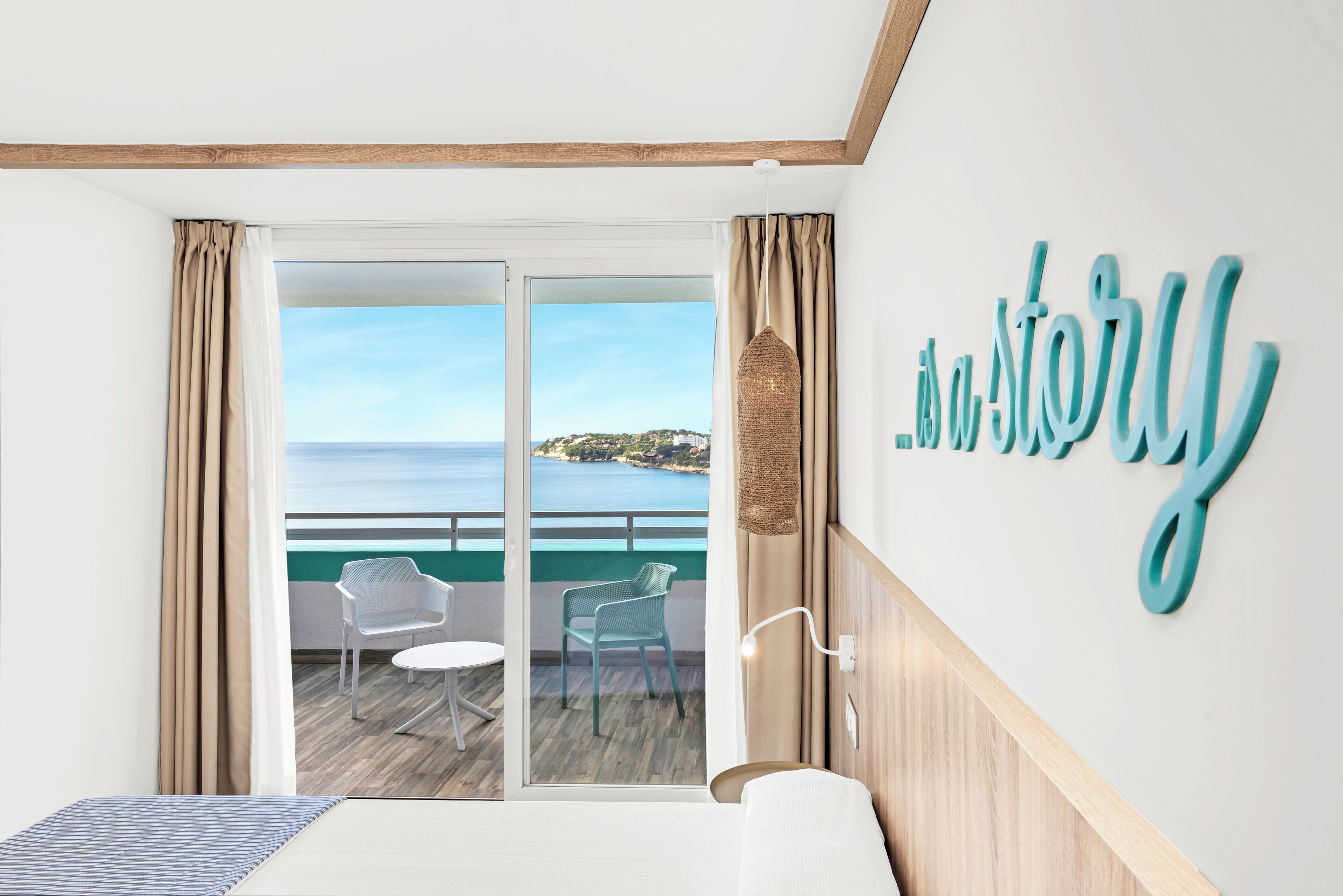 A hotel room with a balcony, a bed, a small table, two chairs, and a decorative wall piece.