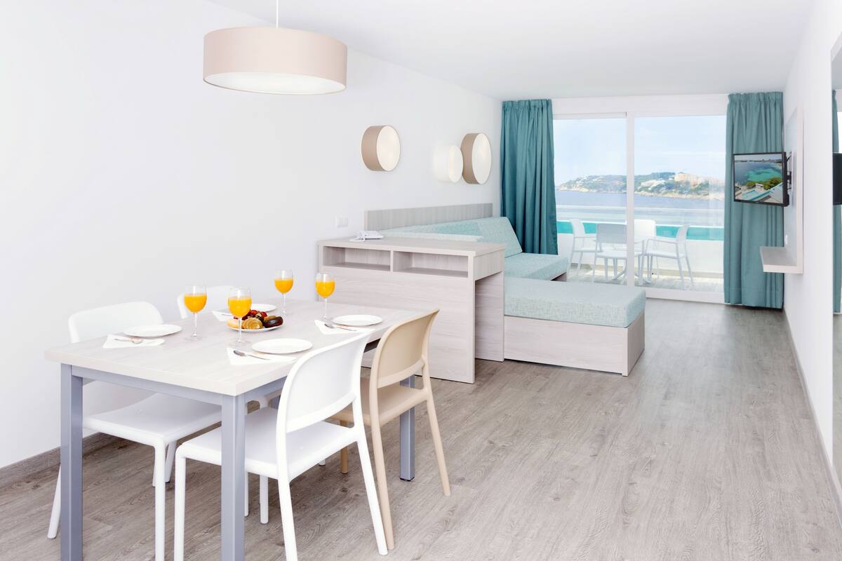 A modern room with a dining area, a bed, and a view of the sea.