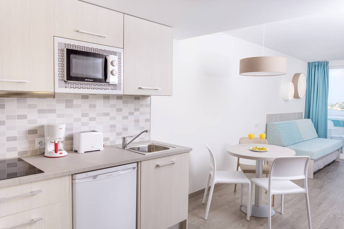 A modern kitchen with a microwave, toaster, and dishwasher. There is a dining area with a table and chairs, and a sofa with a view.