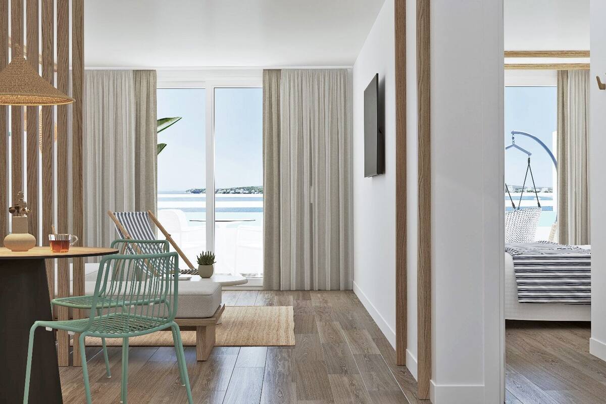 A modern room with a wooden floor, a dining table with chairs, a hanging light fixture, and a view of the sea through large windows.