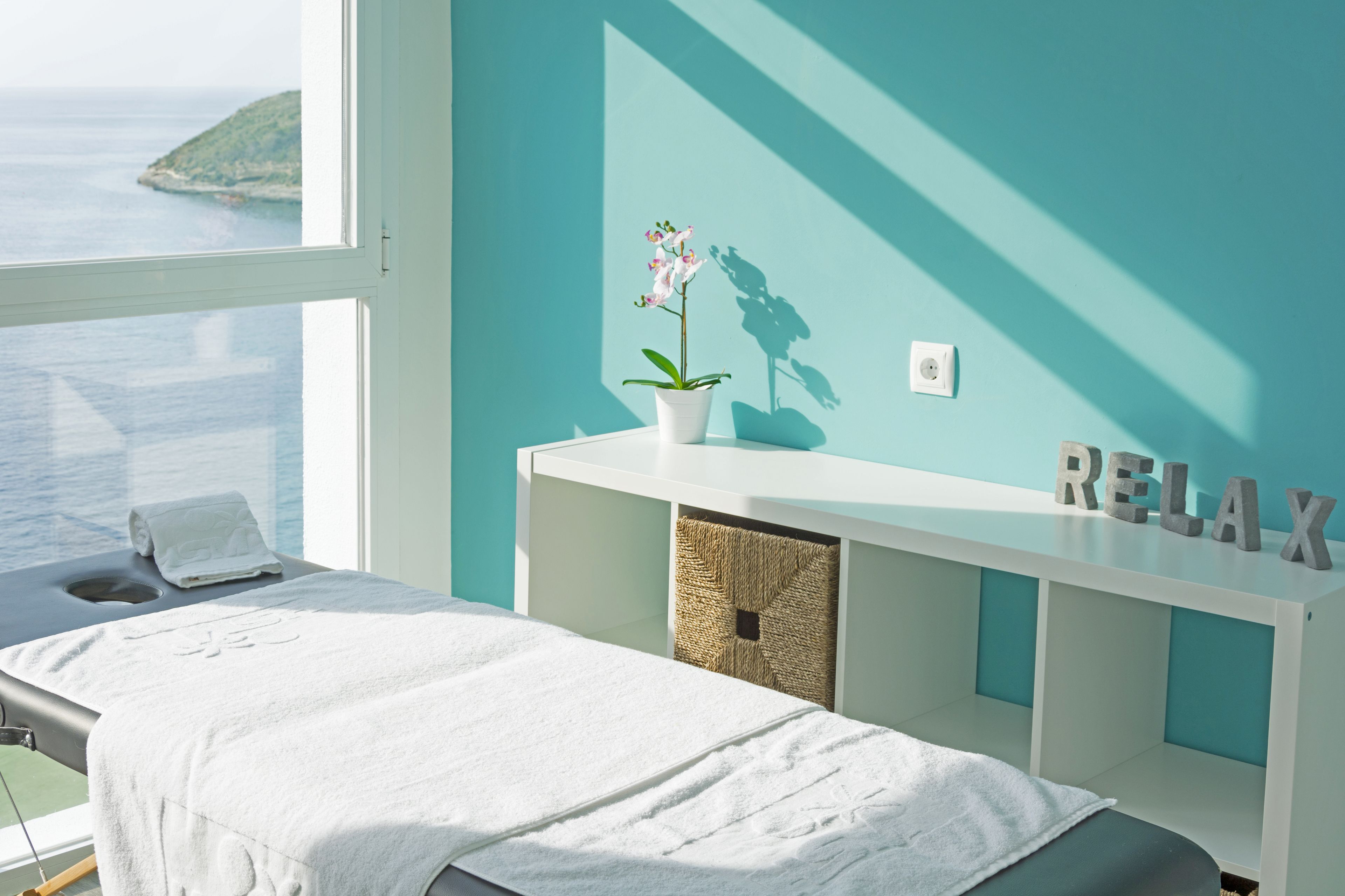 Un cuarto de spa con una camilla de masaje, una orquídea en maceta y una pared con la palabra 'RELAX'.