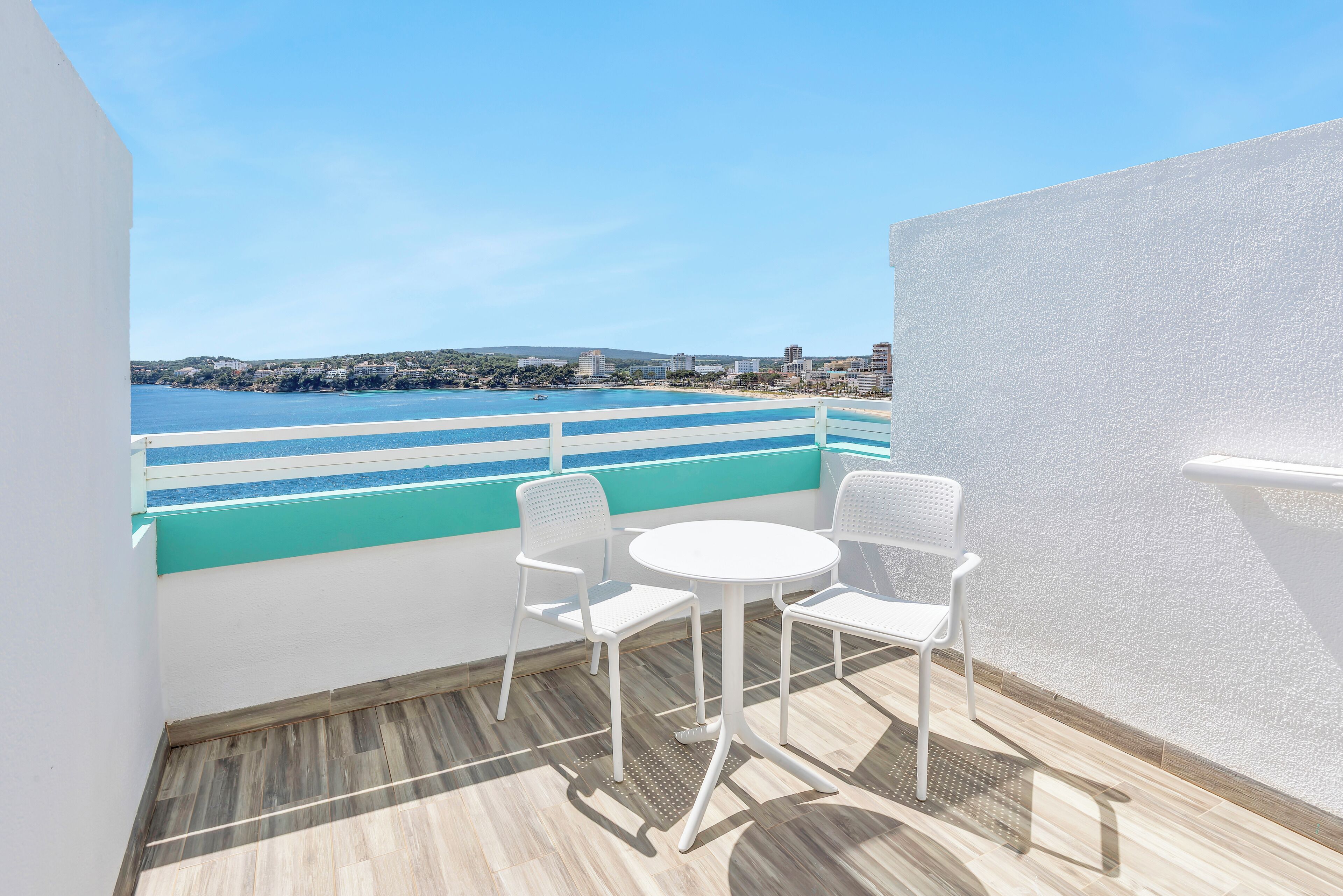 A balcony with a view of the sea, a white table, and two white chairs.