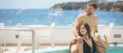 A couple in a swimming pool with a view of the sea and a distant island.