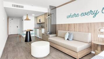 Una sala moderna con un sofá, una mesa redonda, un comedor con sillas y una cocina al fondo.