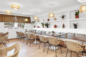 Un interior moderno con muebles de mimbre, una larga mesa de comedor e iluminación colgante.