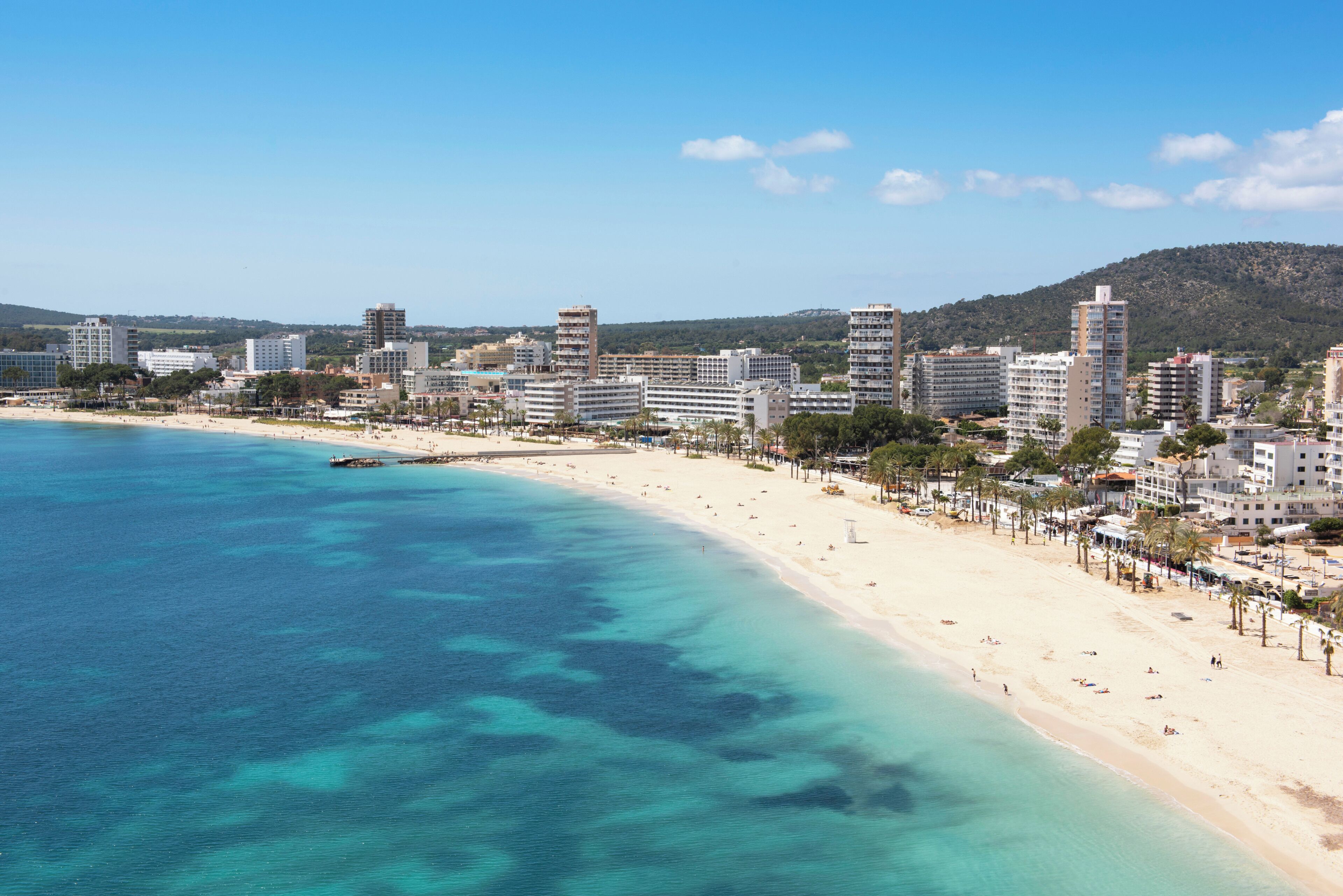 A coastal cityscape with a sandy beach, high-rise buildings, and clear blue waters.