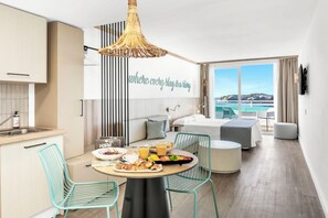 Habitación de hotel moderna con cocina, comedor y un ventanal con vista al mar.